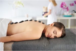 Жена лежи на кушетка с горещи камъни върху гърба по време на масаж.