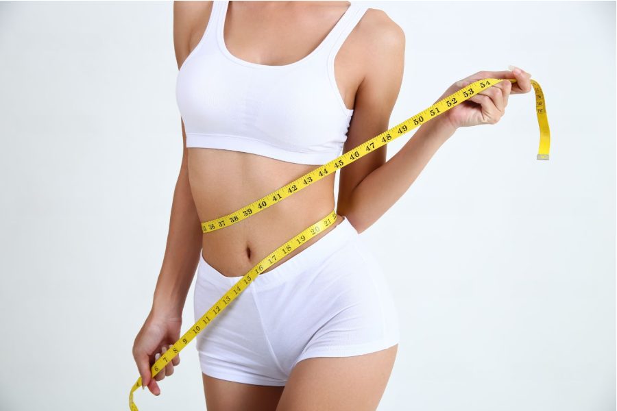Млада жена с красиво тяло измерва обиколката на талията си със сантиметър.