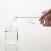 Жена сипва зеолитна вода от стъклено шише в чаша