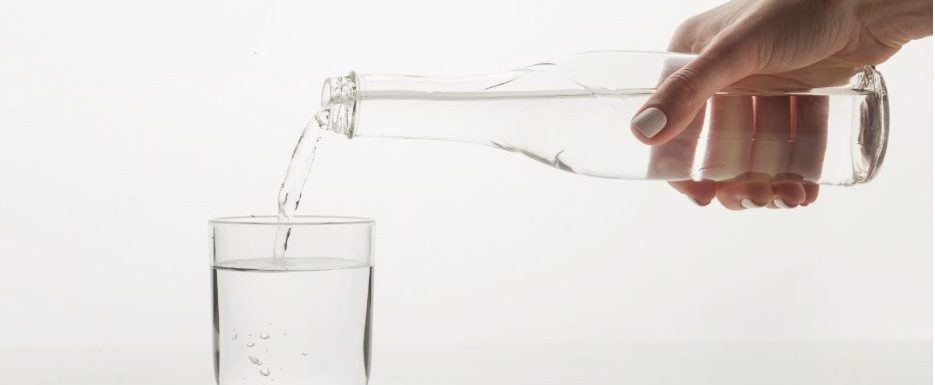 Жена сипва зеолитна вода от стъклено шише в чаша