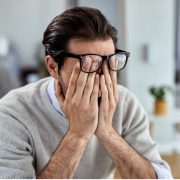 Мъж с очила, който прикрива очите си с ръце и изглежда стресиран